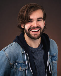 Headshot of Noah Sisson in a jean jacket, smiling.