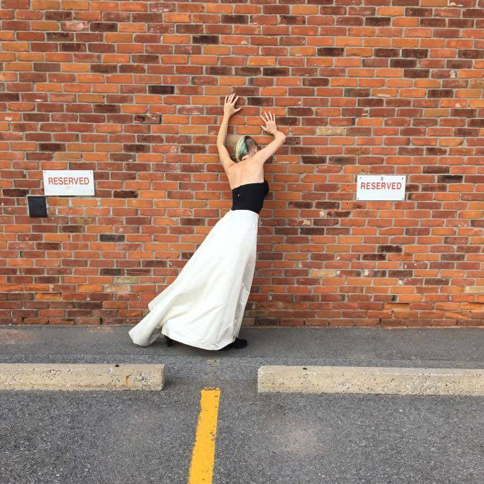 photo shot from behind of Kate Story with her hand on a brick wall in a parking lot
