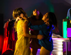 3 performers standing in a circle with arms on each others shoulders.