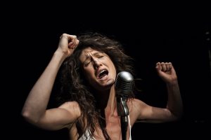 Amy Nostbakken performing in front of a microphone with arms raised.