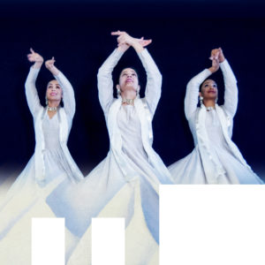 3 dancers in white robes with arms raised.