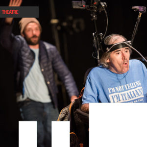 Two actors, one faded into the background and the second actor is in the front in a chair with a electronic headpiece on.