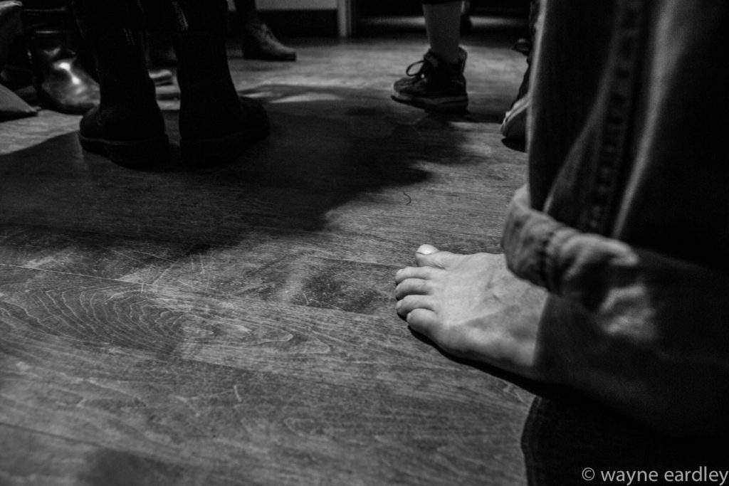 Bare feet of audience on Market Hall floor. In Greyscale.