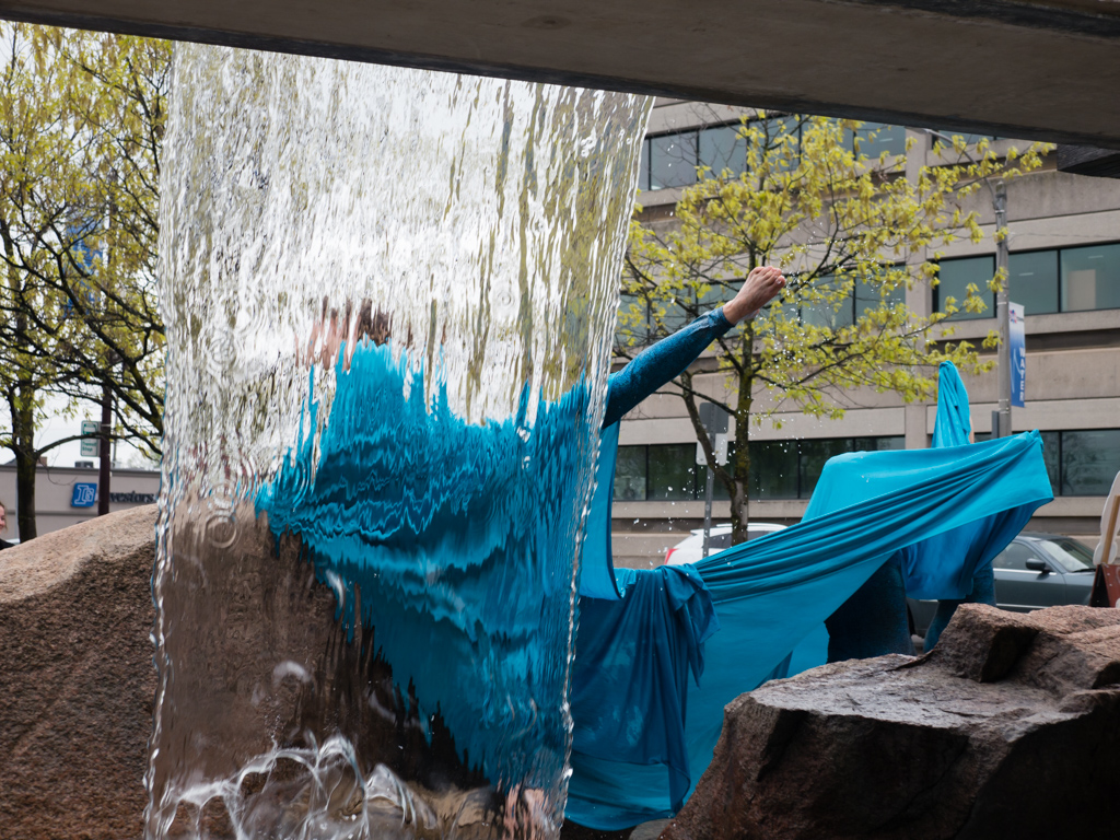Photo of a waterfall with people huddled under a blue silk in front