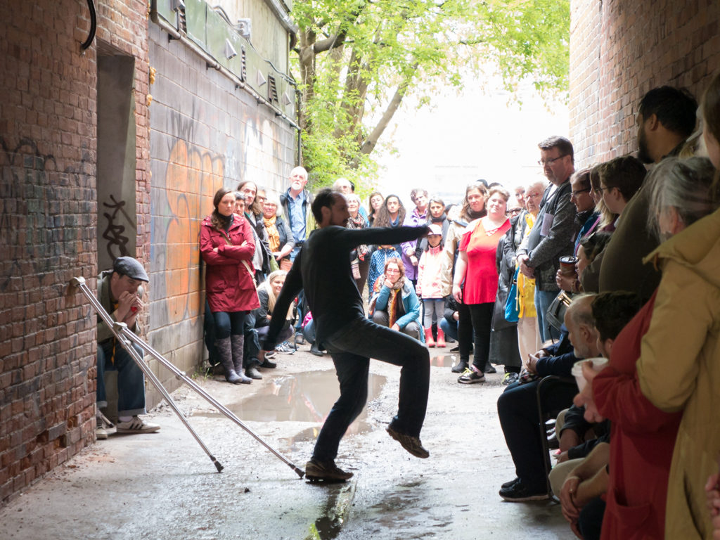 Photo of Wes Ryan performing in alley (audience in the background)