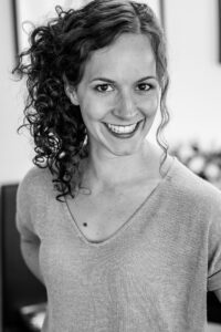 A black and white photo of a woman. She is smiling and her curly hair is pulled into an updo.