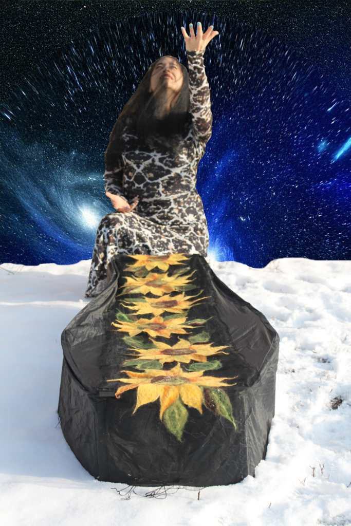 Heryka raises one arm to a starry sky, crouched in the snow over a coffin draped in a string of textile sunflowers.